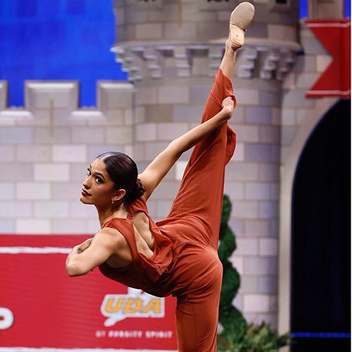 Iona Dance Team member performing on stage, doing a dance move where she's leaning forward and holding her leg up behind her.