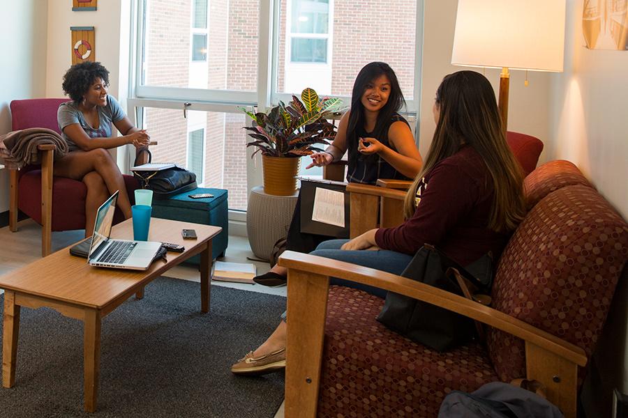 Three female students talk in a common area of a dorm room.