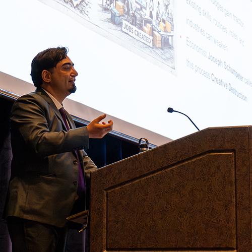A close-up shot of Dr. Aakash Sapru speaking at a wooden podium during a presentation.