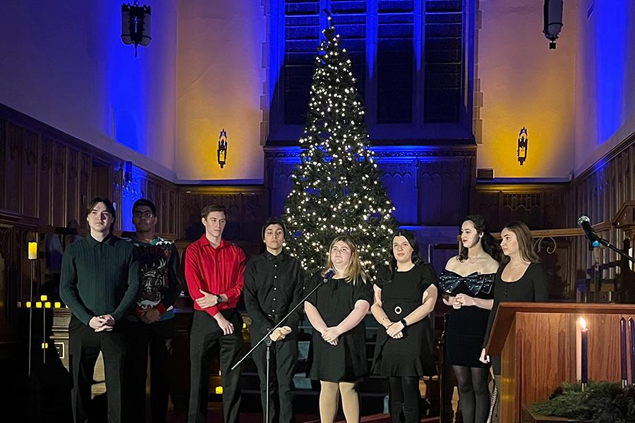 Singers sing on stage in front of a lit Christmas Tree.