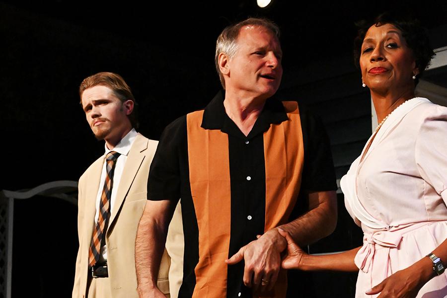 A man holds a woman hand and speaks to her while another man looks off in the distance.