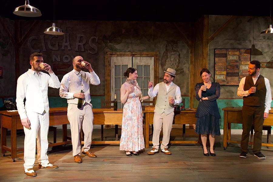 People stand and talk on stage while drinking in Anna in the Tropics.