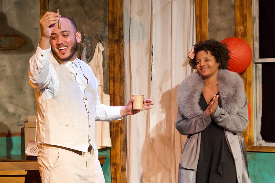 A male actor raises a cigar and smiles with a female actor looking on smiling in Anna in the Tropics.