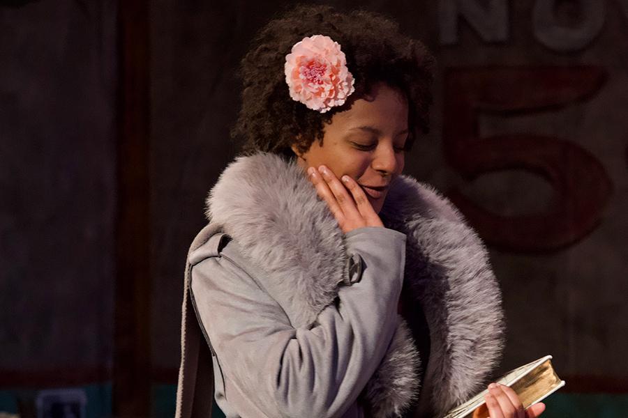 A female actor with a pretty flower in her hair holds a book and smiles in Anna in the Tropics.