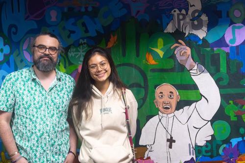 Jidapha Vastola ’27 and Dr. Jim Robinson standing and smiling next to the mural.