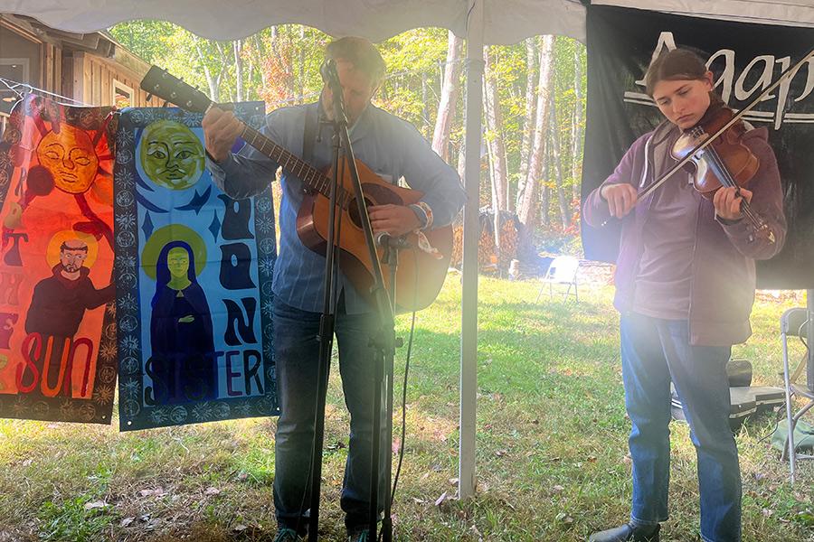Two musicians are playing music outside, while the two banners, entitled “Brother Sun, Sister Moon,” are hanging in the background for display.