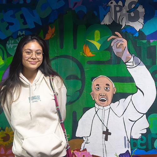 Jidapha Vastola ’27 standing next to the Earth & Spirit Mural.