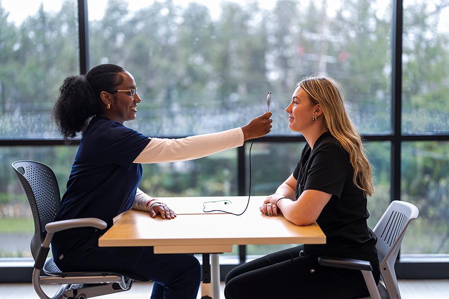 Two nursing students sitting, practicing and checking eye vision inside a classroom.