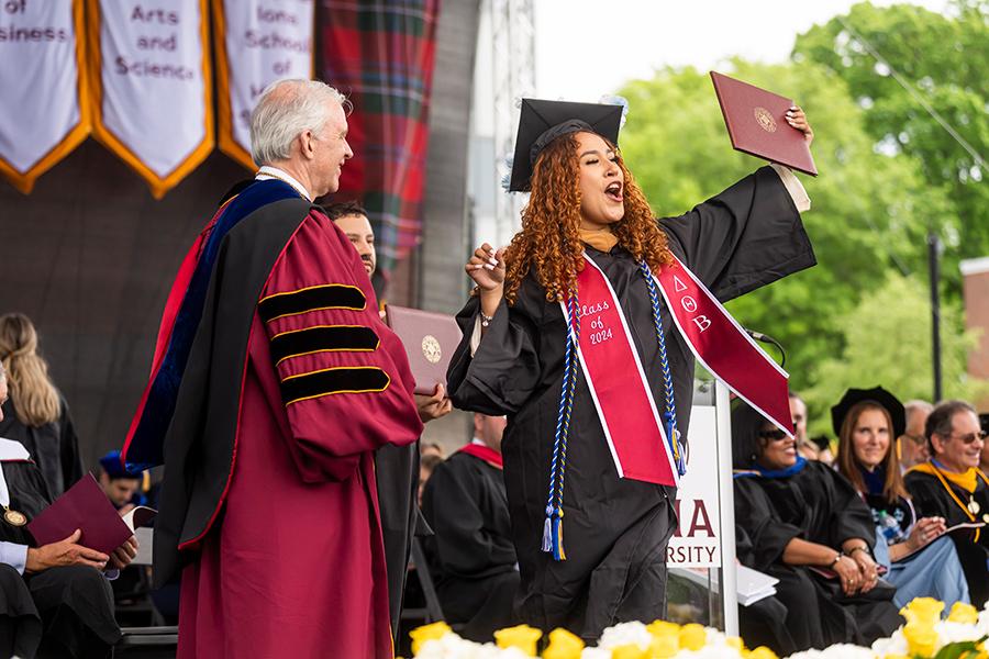 Student, on stage, cheering after receiving her diploma at the Iona University 80th Annual Commencement Ceremony.