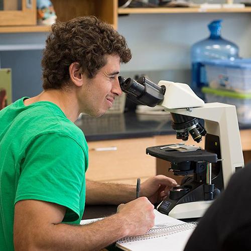 A student in a green shirt works with a microscope in the biology lab.