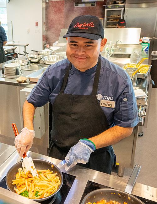 The chef at the pasta station cooks and smiles.