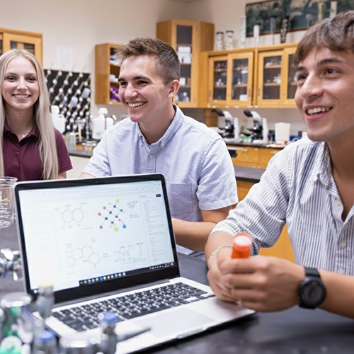 Three chemistry students in the lab with a laptop.