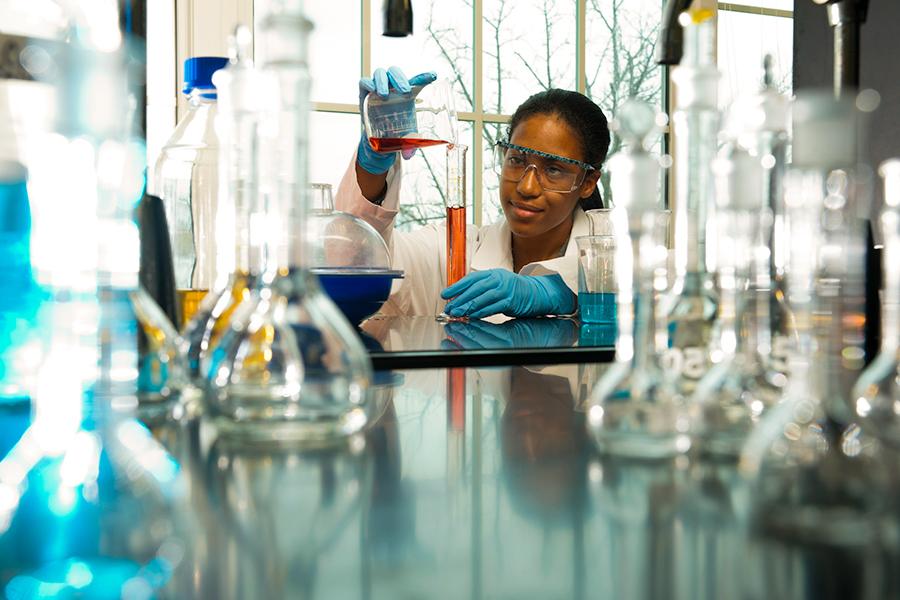 A chemistry student pours liquid from a beaker into a graduated cylinder.