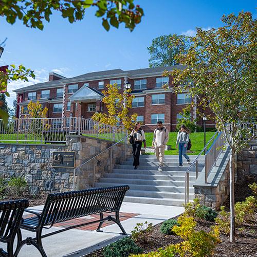 Three students are outside walking down the stairs near the Murphy Green.