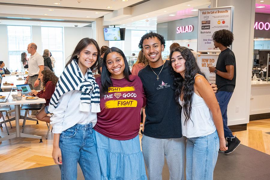 Four students smiling and posing together inside the brand new dining hall, Student Union.