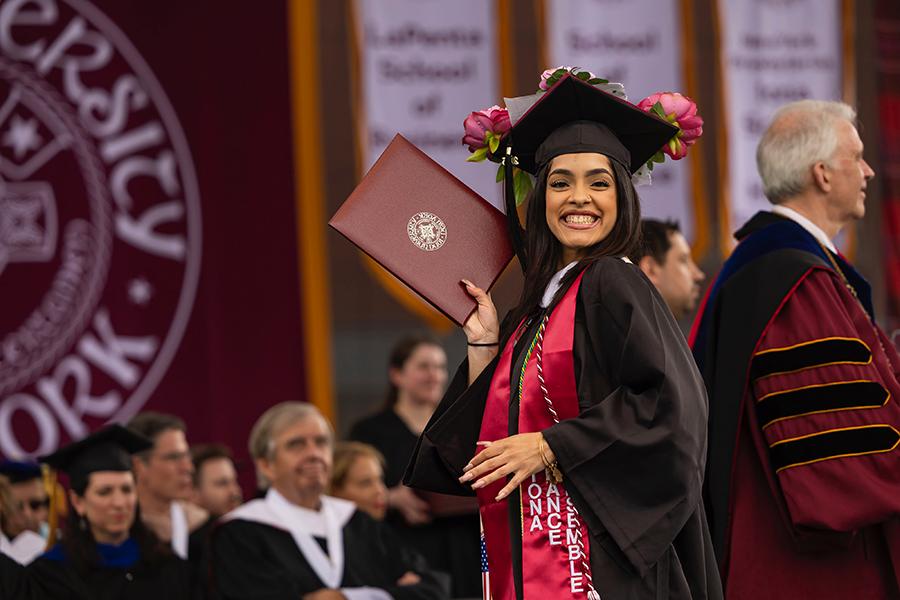 A grad smiles with her degree and walks across the stage.