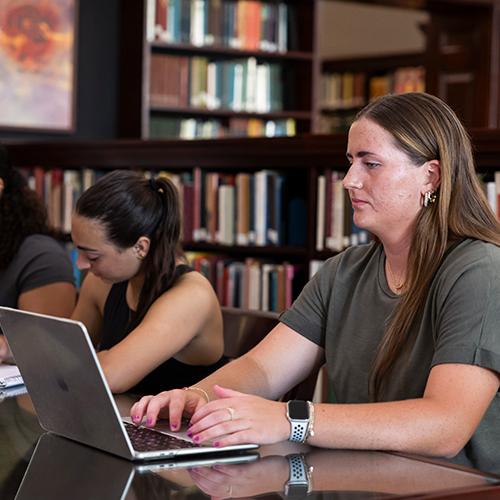 A graduate student works on her laptop in the library.
