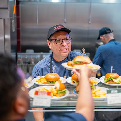 A chef hands a burger with fries to a student in the new dining hall.