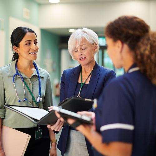 A healthcare leader and two doctors discuss something in the hallway of a hospital.
