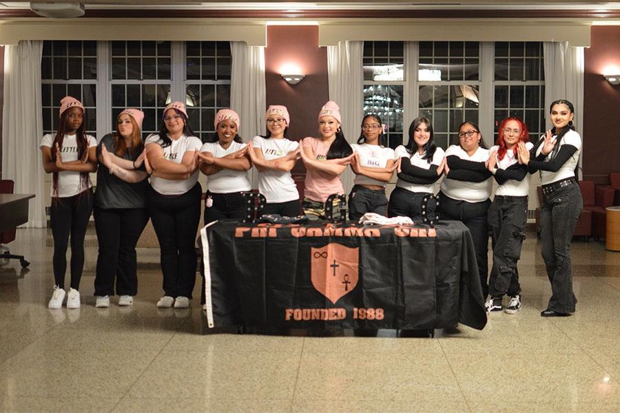 Members of Phi Gamma Chi criss cross arms at their table at a fund raising event.