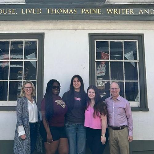 Leanne O’Boyle and Adam Arenson, standing and posing with three students for a group photo in front of the Thomas Paine house in Lewes, England.
