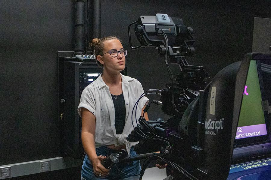 Female student standing behind the camera, filming the live broadcast.