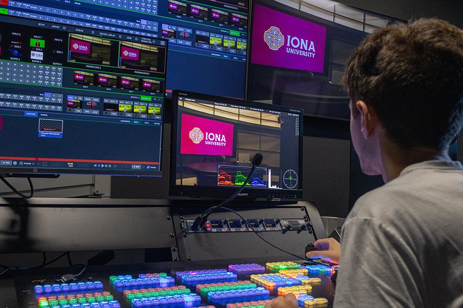 Male student sitting in the soundboard room, looking at several monitors, and adjusting the levels as needed for the live broadcast. 