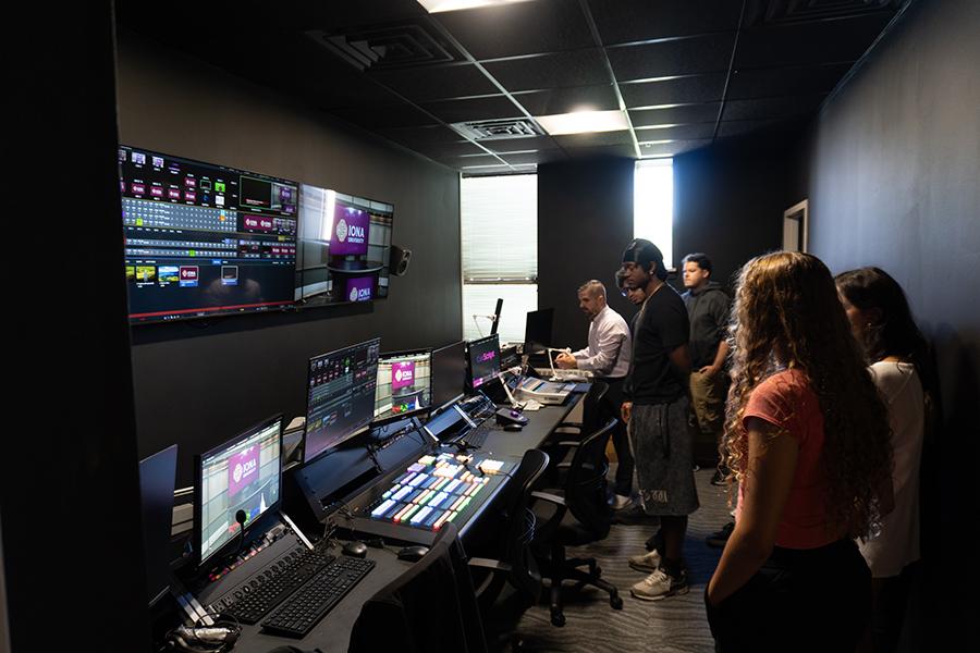 Several students standing, looking over the soundboard controls and monitors.