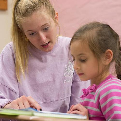 A student teacher helps a young student pronounce words from a book.