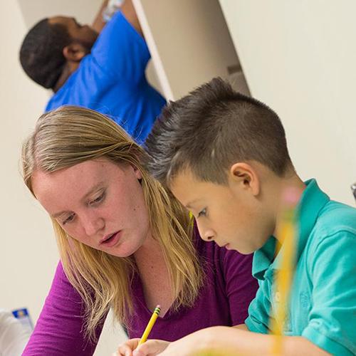 A student teacher helps a young student learn how to write.