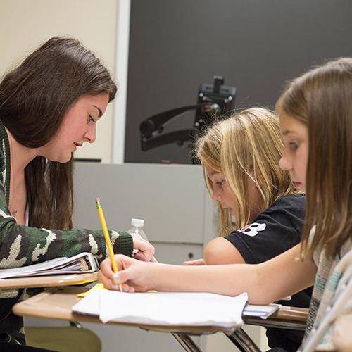 A student teacher works with two young students on their writing.