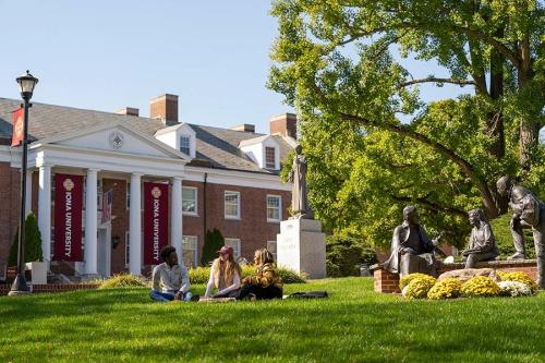 Three students sit on a sunny lawn in front of McSpedon Hall.