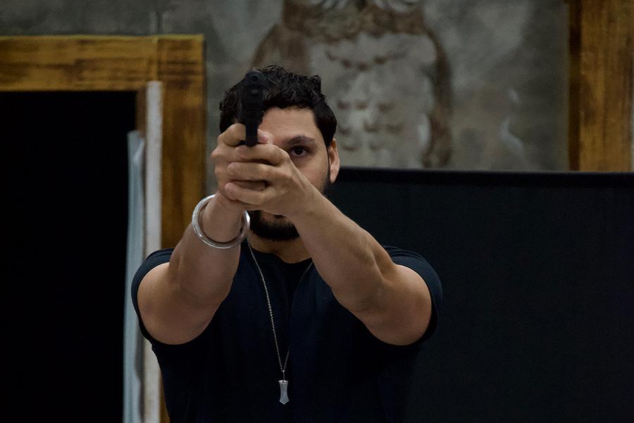 Male actor, holding and pointing a weapon, during the performance of "Motherland" by Iona University's Theatre Ensemble.