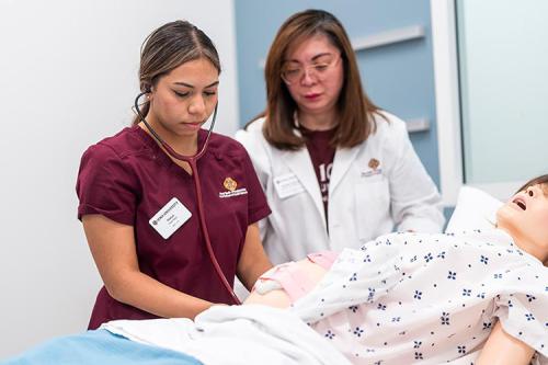 A nursing student works with a professor on a health care mannequin.