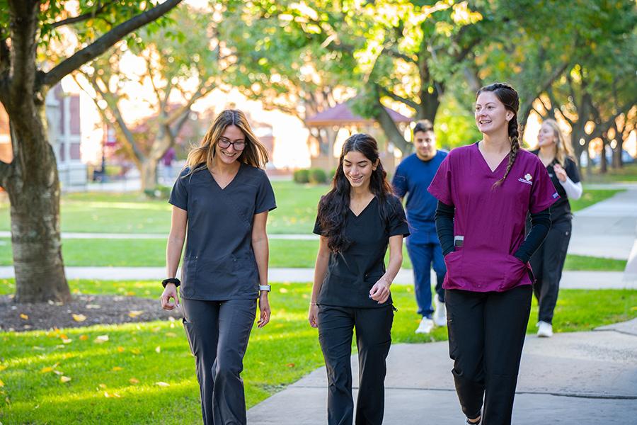 Nursing students walk near the Kelly Center for Health Sciences on a sunny day.