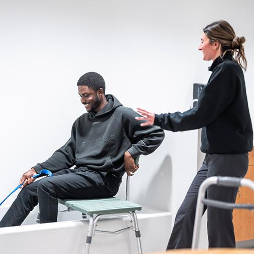 Two OT students practice helping a patient get out of the bathtub.