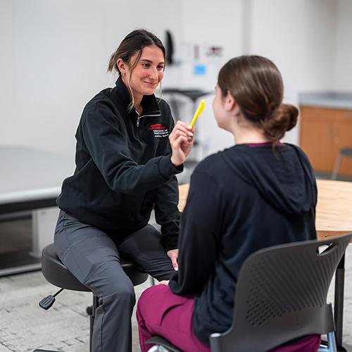 Two OT students practice helping a patient with vision.