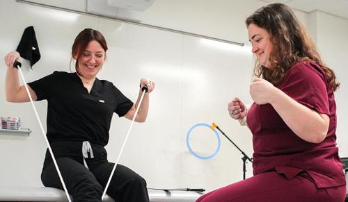 Two OT students practice assisting with putting on socks using a band.