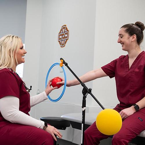 Two OT students practice movements with a ball.