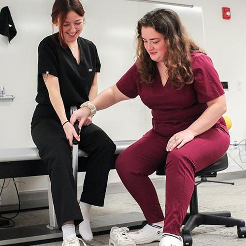 Two OT students practice assisting with putting on a shoe using a band.