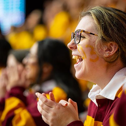 A student in the pep band smiles and claps at a game.