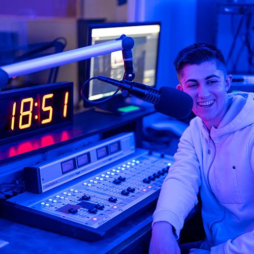 A student in the podcast studio smiles on the mic.