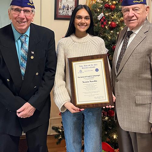 Two veterans stand with Nestrin Nuredin as she displays her award.