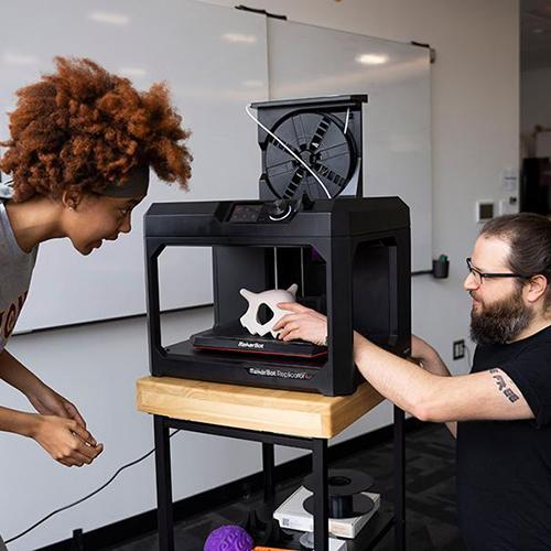 A professor and a student work with a 3D printer.