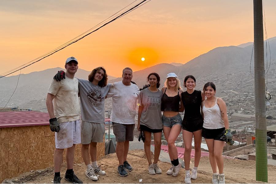 The members of the Iona Mission Trip, posing for a group photo on a hill with the sun setting in the background.
