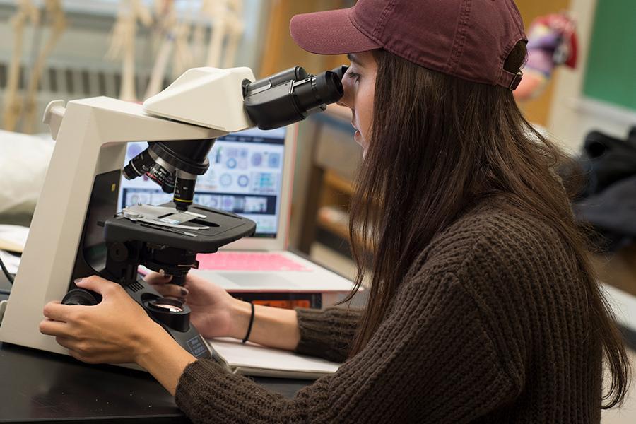 A student in a baseball cap works at a microscope.