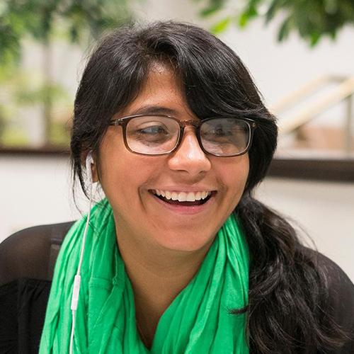 A student in a green scarf smiles on a bench on campus.