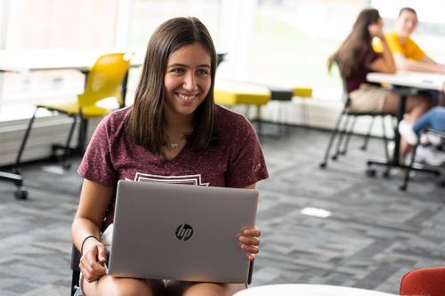 A student with a laptop smiles. 