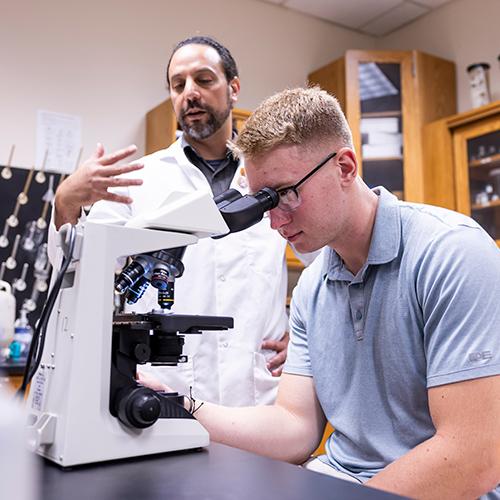 A student and a professor work with a microscope in the chemistry lab.