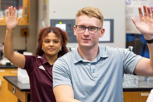 Two students raise their hands in Chemistry class.